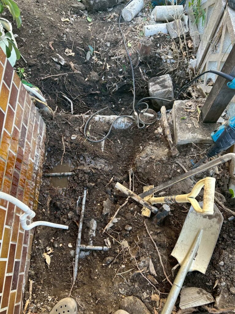 地面を掘っている最中の軒下の様子。レンガの塀のそばで地面を掘り進め、水道管のある場所を確認